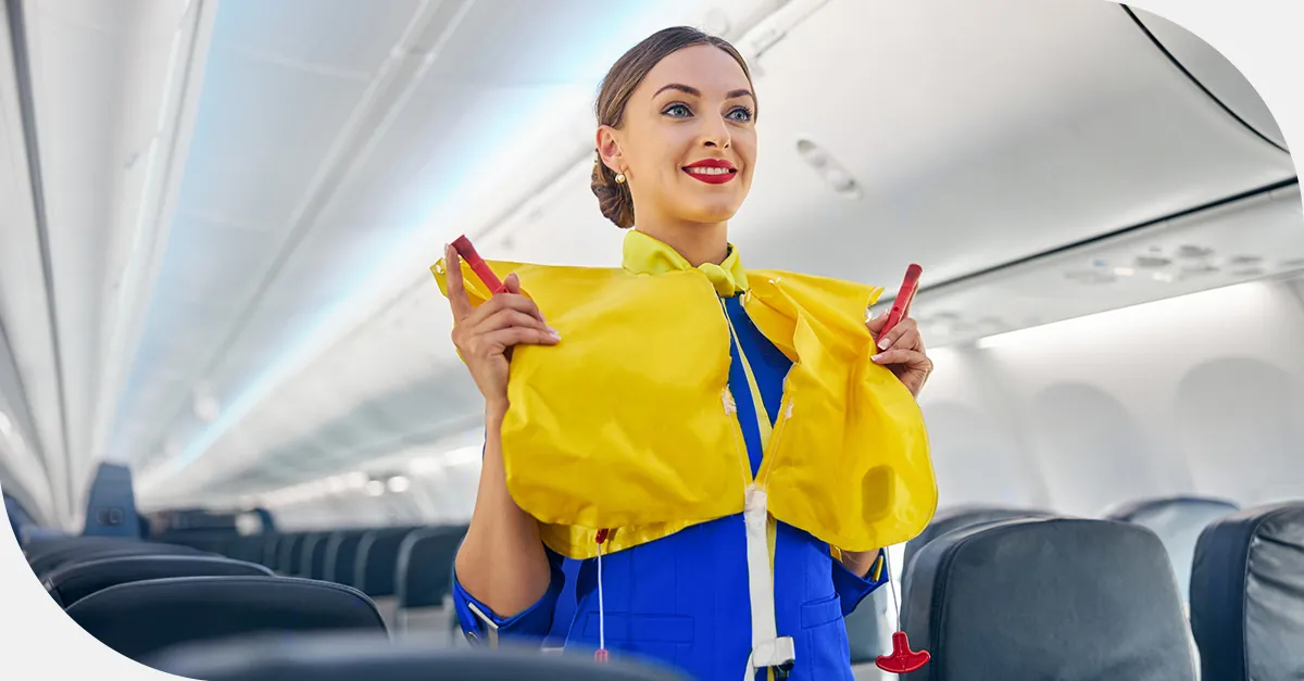Flight attendant demonstrating the use of a yellow life vest inside an airplane cabin.
