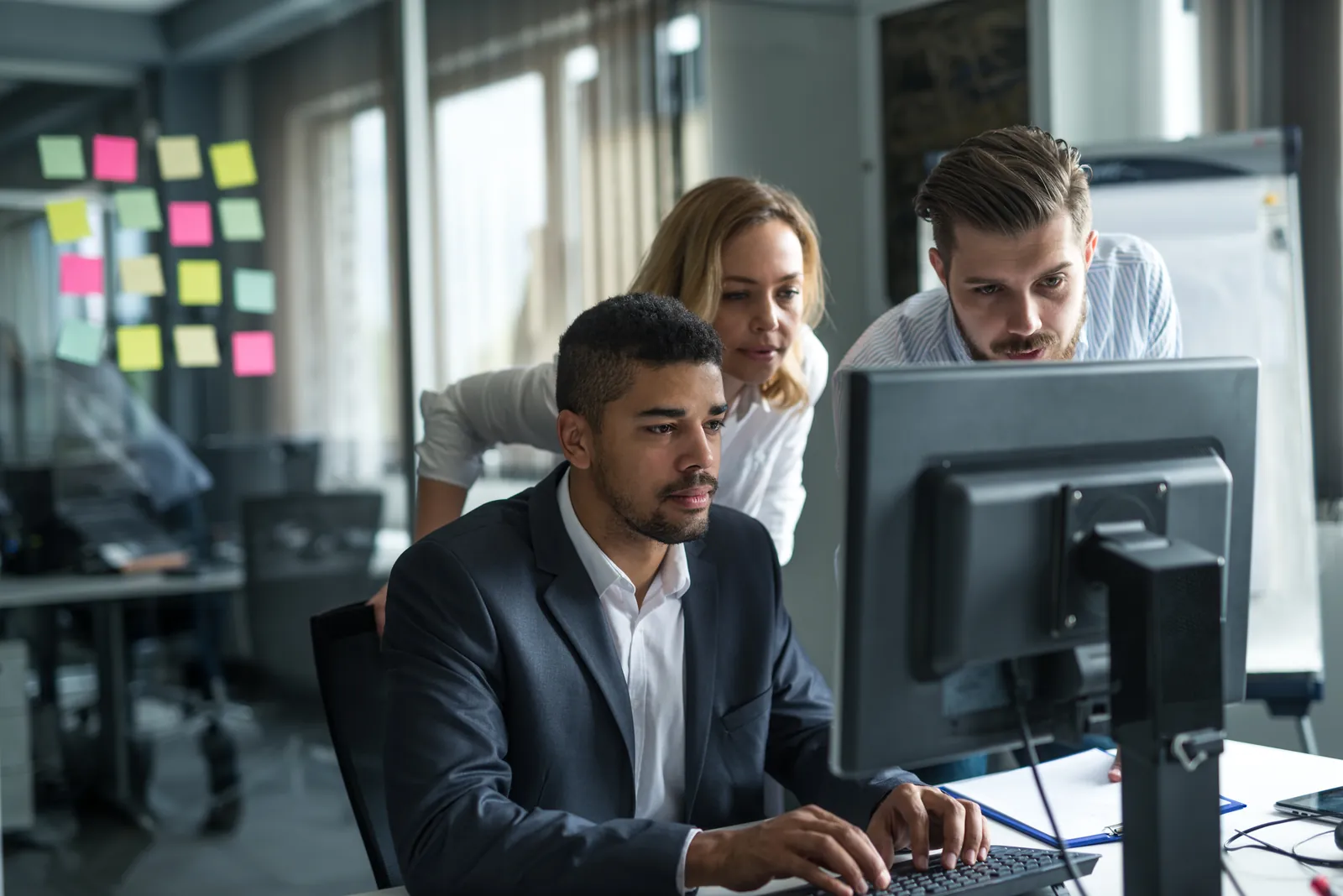 Three professionals collaborating and focusing on a computer screen in a modern office environment.