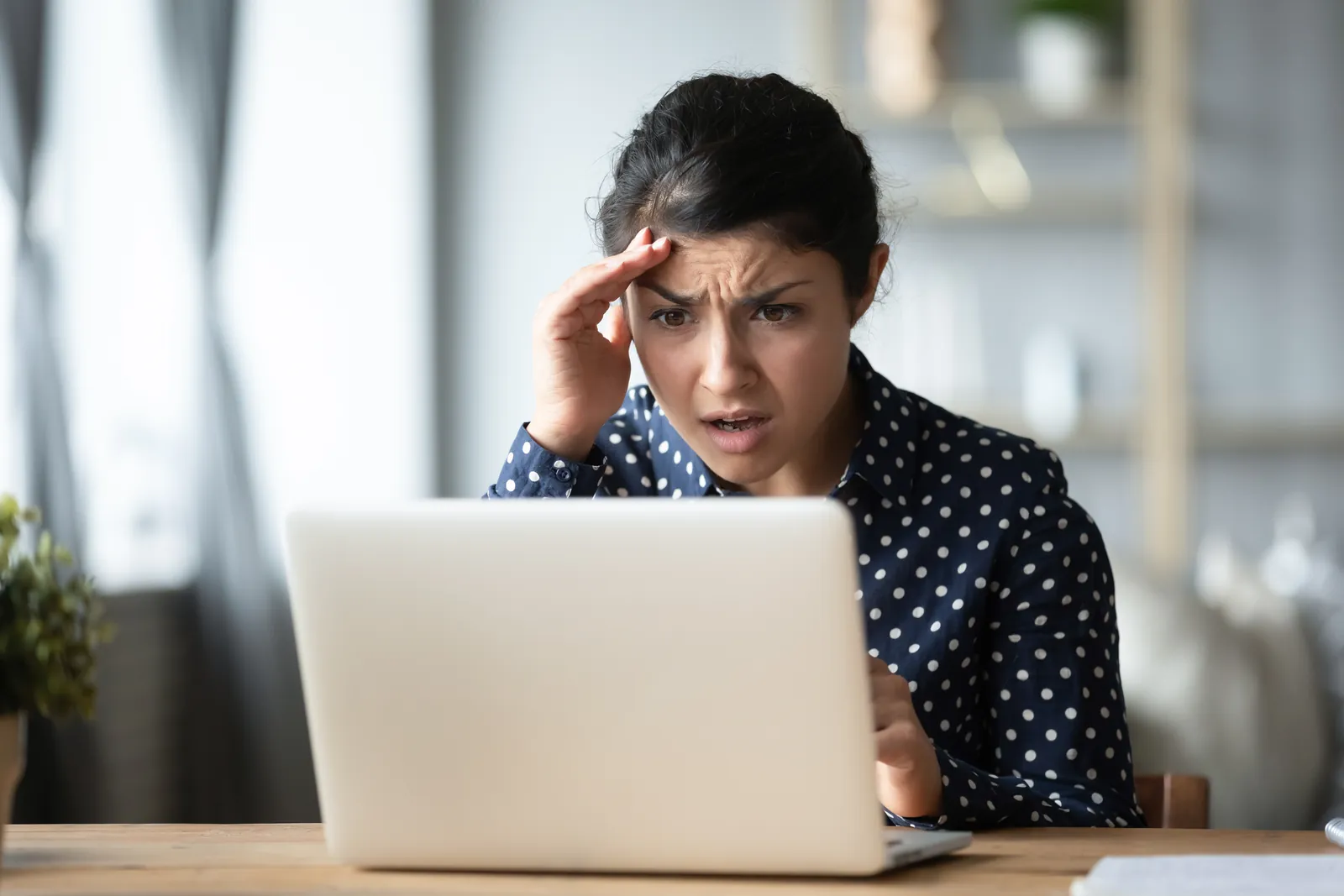 carlsbad-managed-it-services-photo Worried woman in polka dot shirt looking stressed at laptop screen at home desk