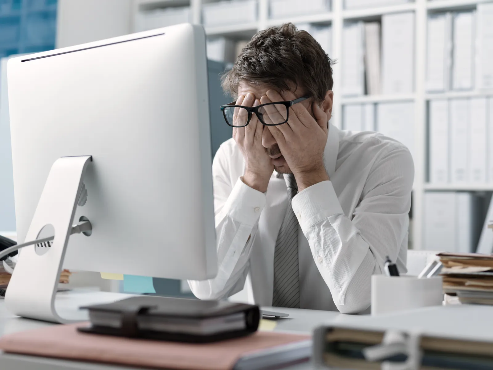 el-cajon-managed-it-services-photo Stressed businessman sitting at desk in front of computer with hands covering his face in office.