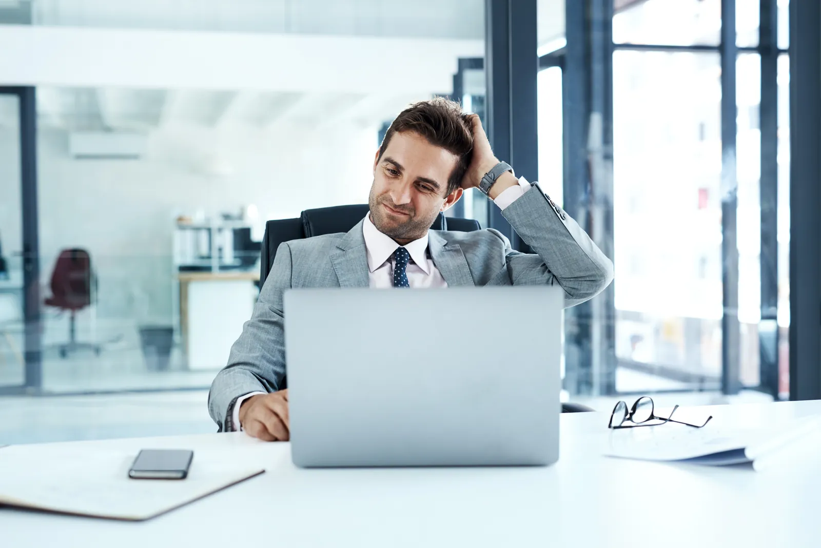 escondido-managed-it-services-photo Businessman in gray suit working on laptop in modern office with documents and smartphone on desk