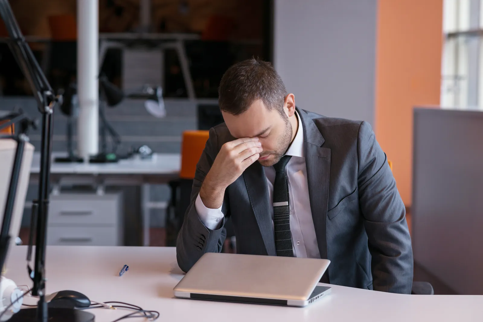 Man with glasses concentrating thoughtfully on laptop screen at home office desk with plant nearby