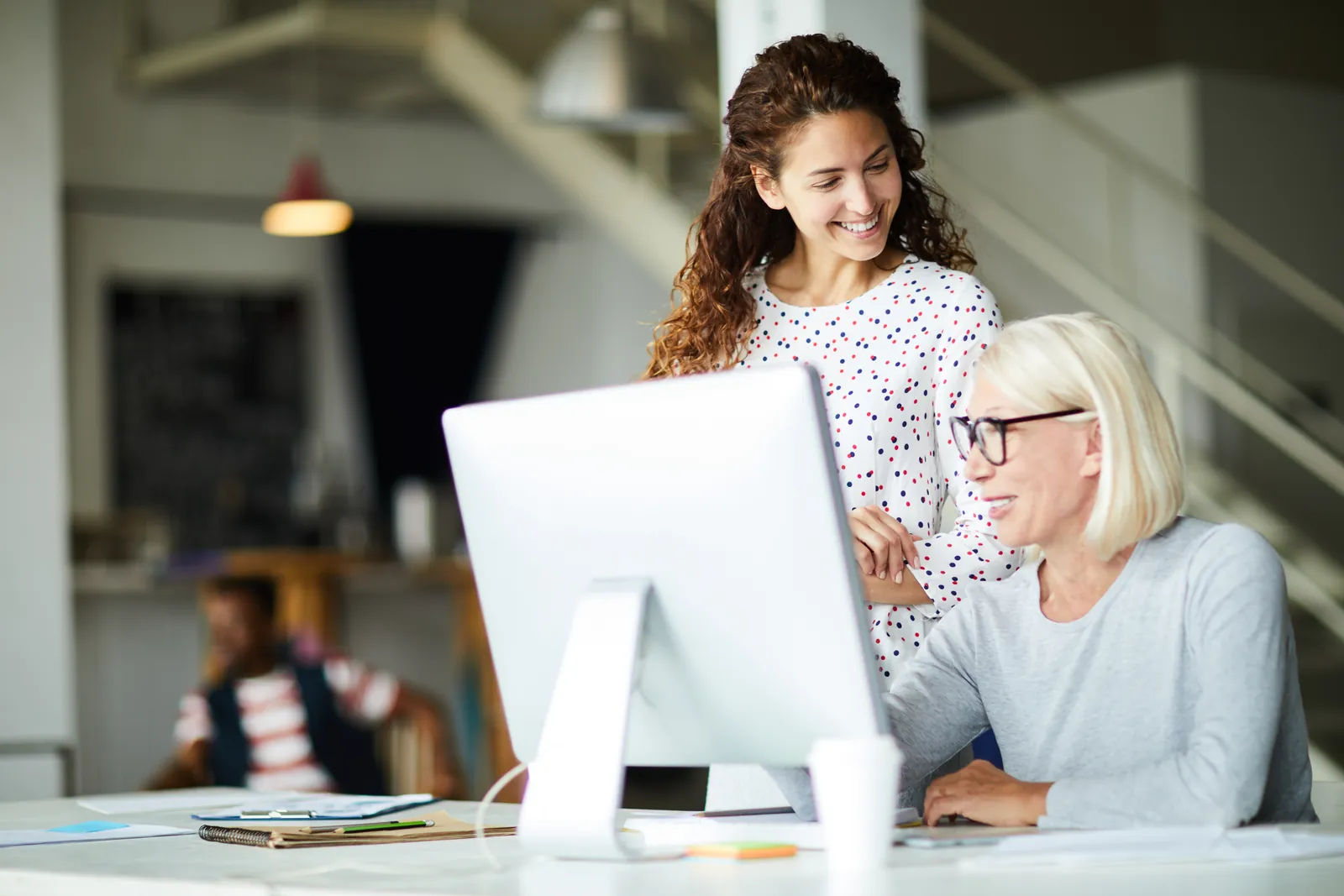 Two women collaborating happily at a computer in a modern bright office environment