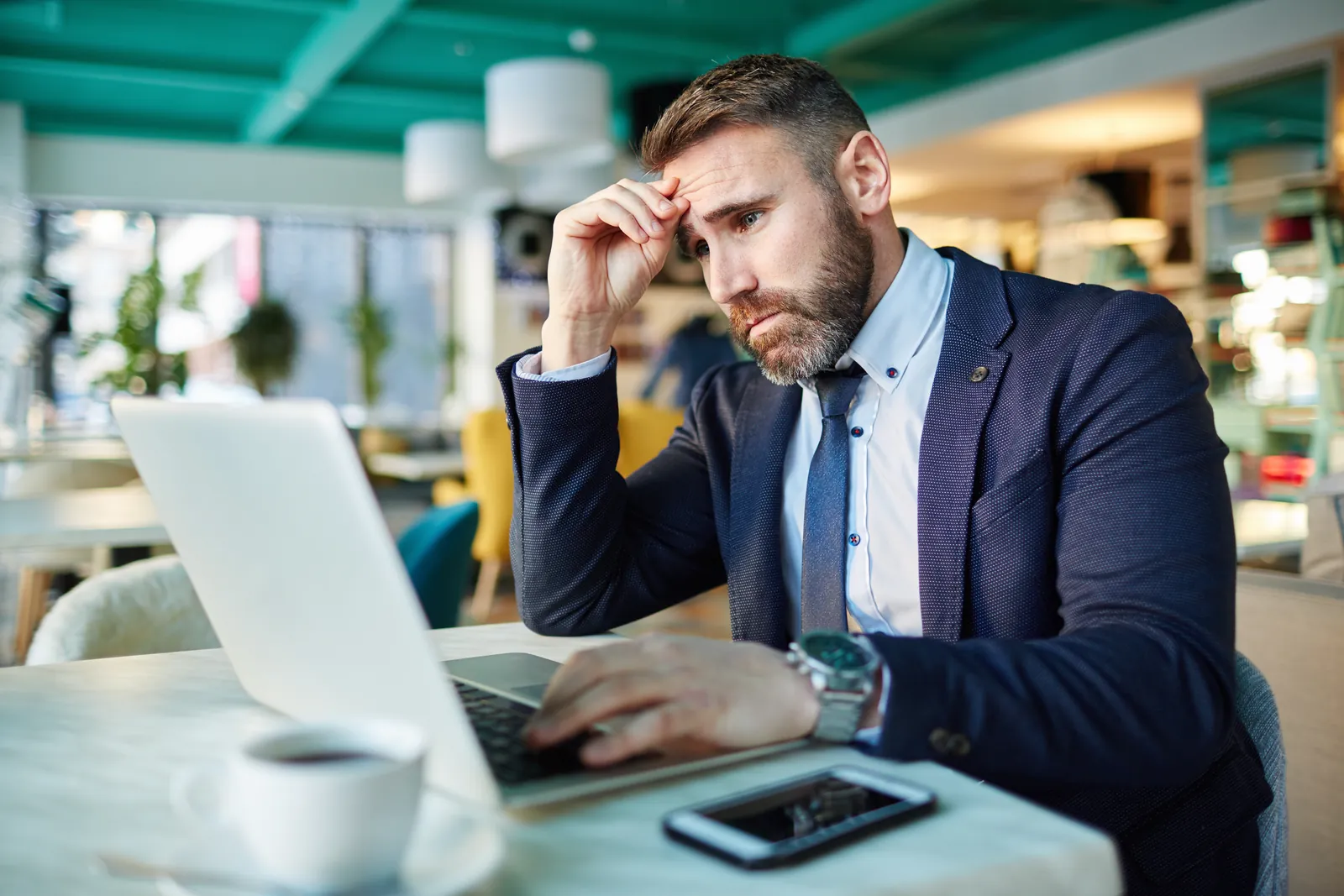 santee-managed-it-services-photo Businessman in suit working on laptop in cafe, looking stressed and focused during work.